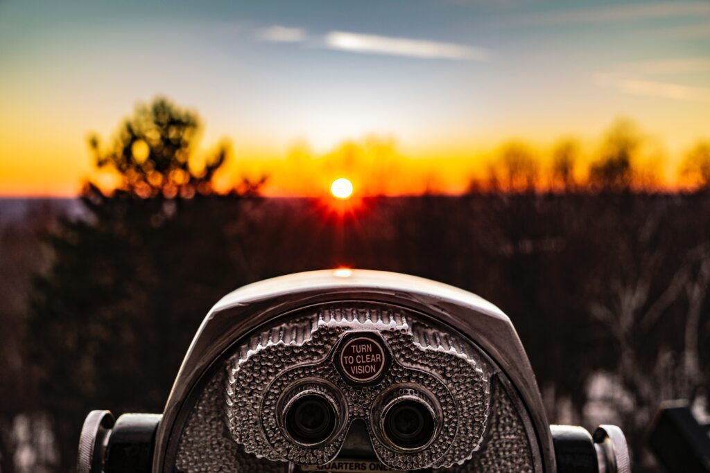 binoculars looking over a sunset horizon with silhouettes of trees